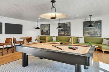 A pool table is in the middle of a room with a green couch and a TV mounted on the wall.